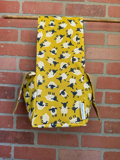 Yellow fabric bag with black and white sheep pattern hanging against a brick wall